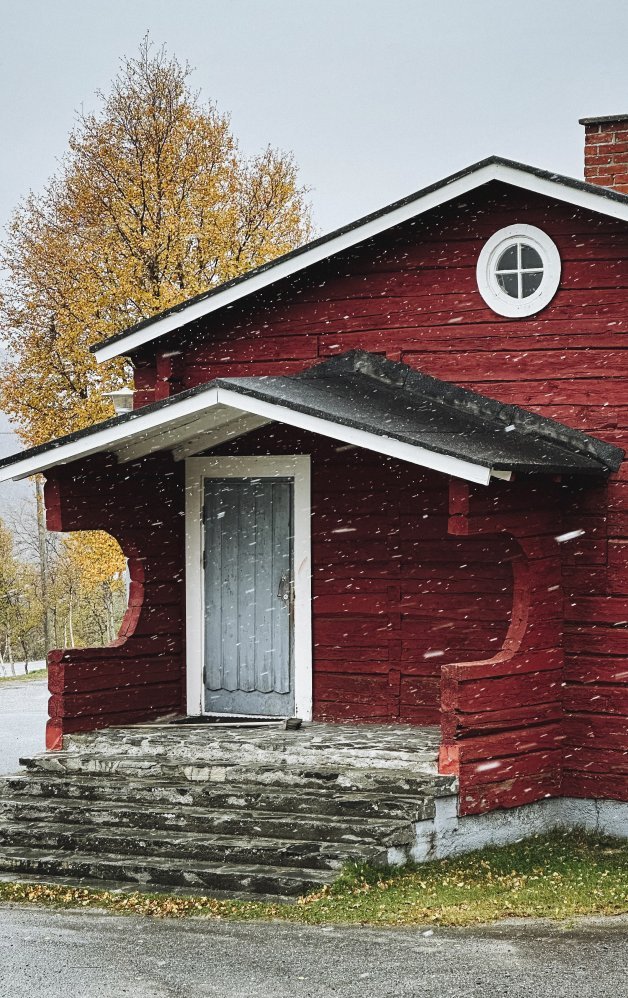 Kuvassa on Retkeilykeskuksen päärakennuksen vanha osa Siilastupa ulkoa päin, lunta sataa, taustalla koivun lehdet ovat oransseja.